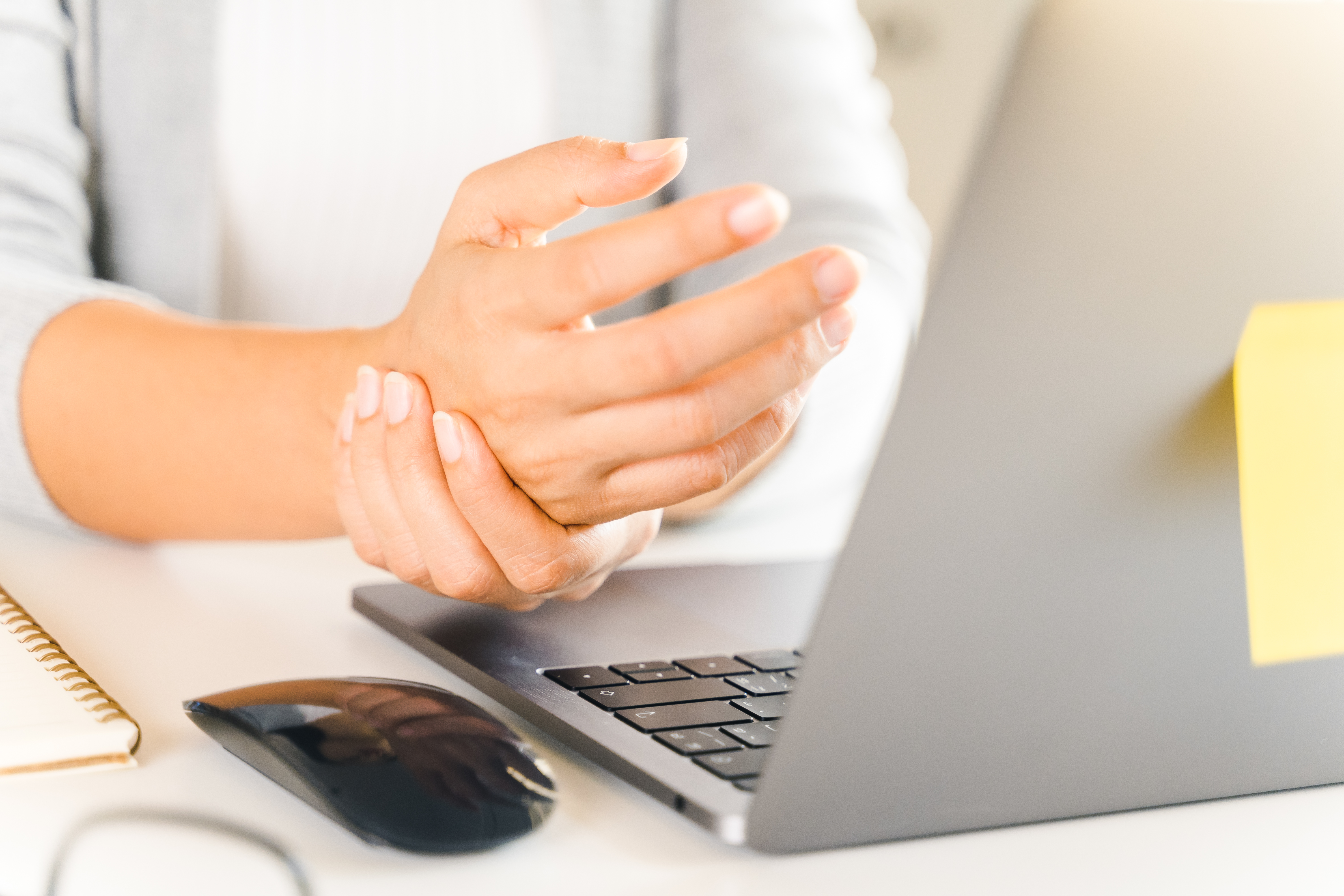 Close-up of a person holding their wrist while working on a laptop — office syndrome