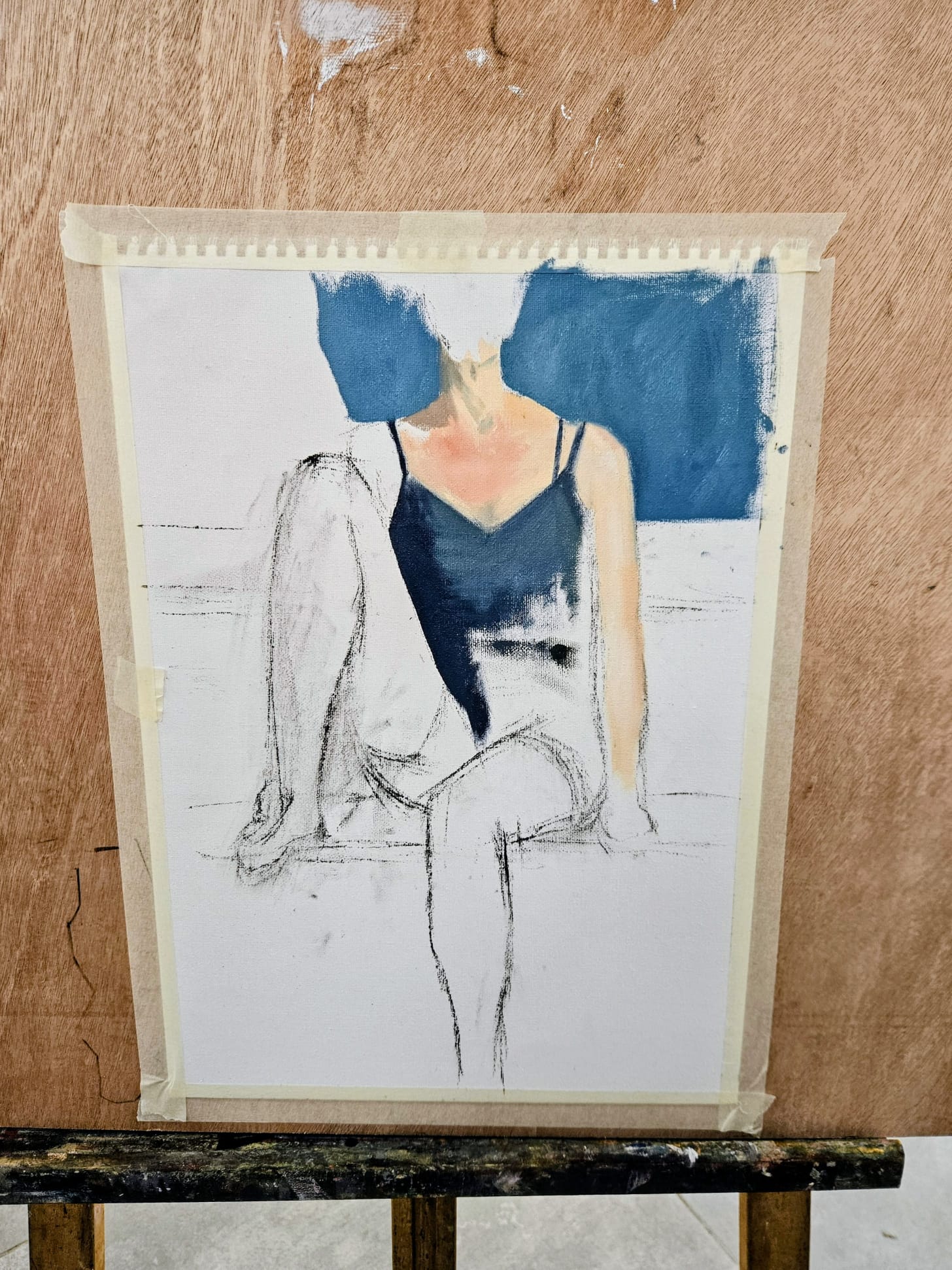 A loose charcoal-and-blue-paint figure study on paper, taped up, resting on an easel.